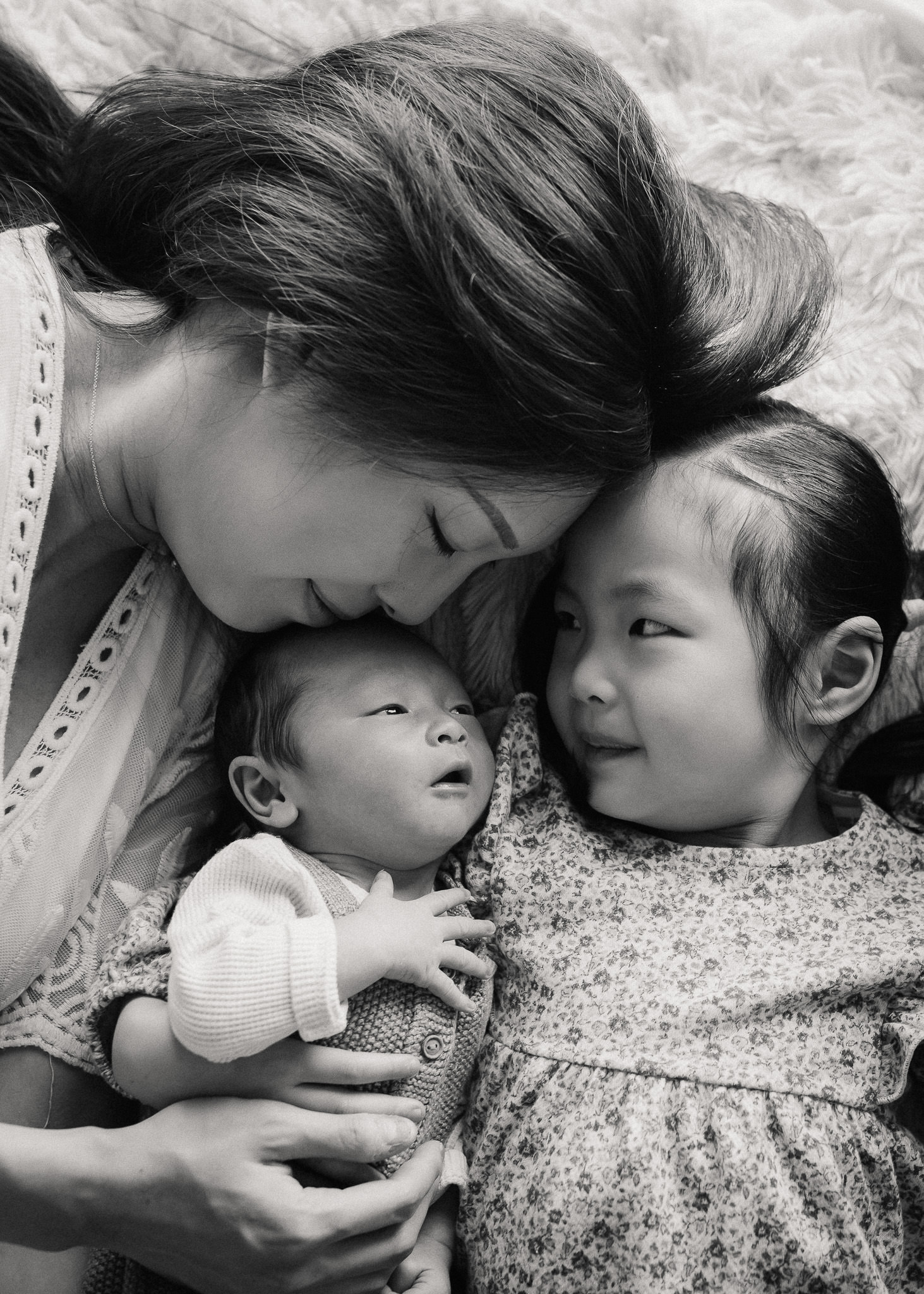 Black and white photo by Ashley Kaplan of mom, toddler and newborn snuggled