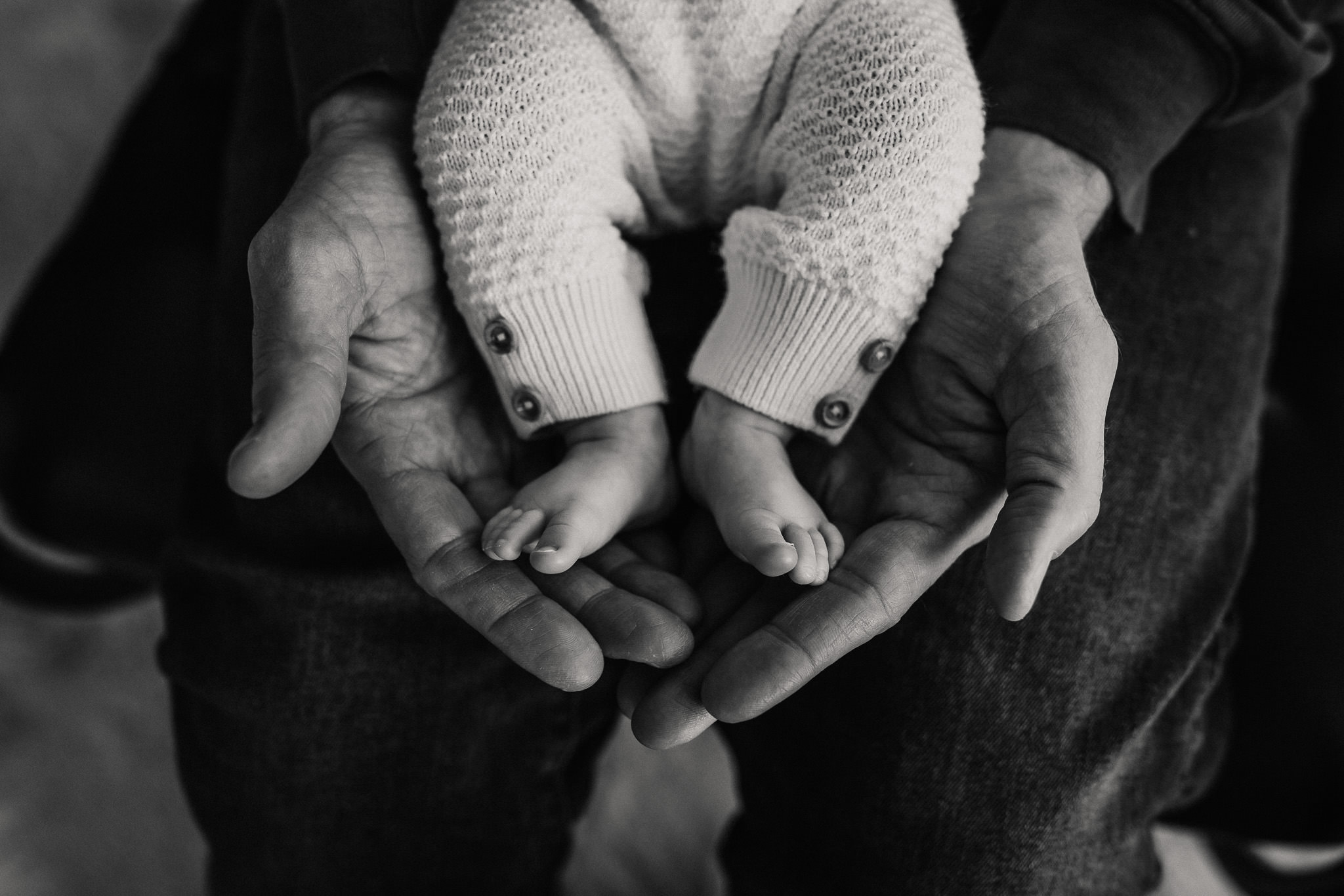 black and white photo of baby feet cupped in dad's hands by Ashley Kaplan Photography